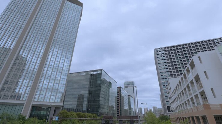 A low-angle shot of modern glass skyscrapers and buildings in Tokyo's Toyosu area against an overcast sky
