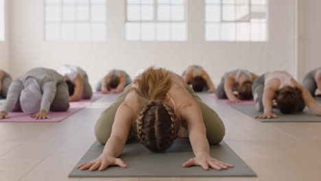 Attraktiver-Yoga-Kursleiter,-Der-Die-Gruppenmeditation-Leitet-Und-Gesunde-Frauen-In-Kinderpose-Unterrichtet-Und-Das-Training-Im-Fitnessstudio-Bei-Sonnenaufgang-Genießt