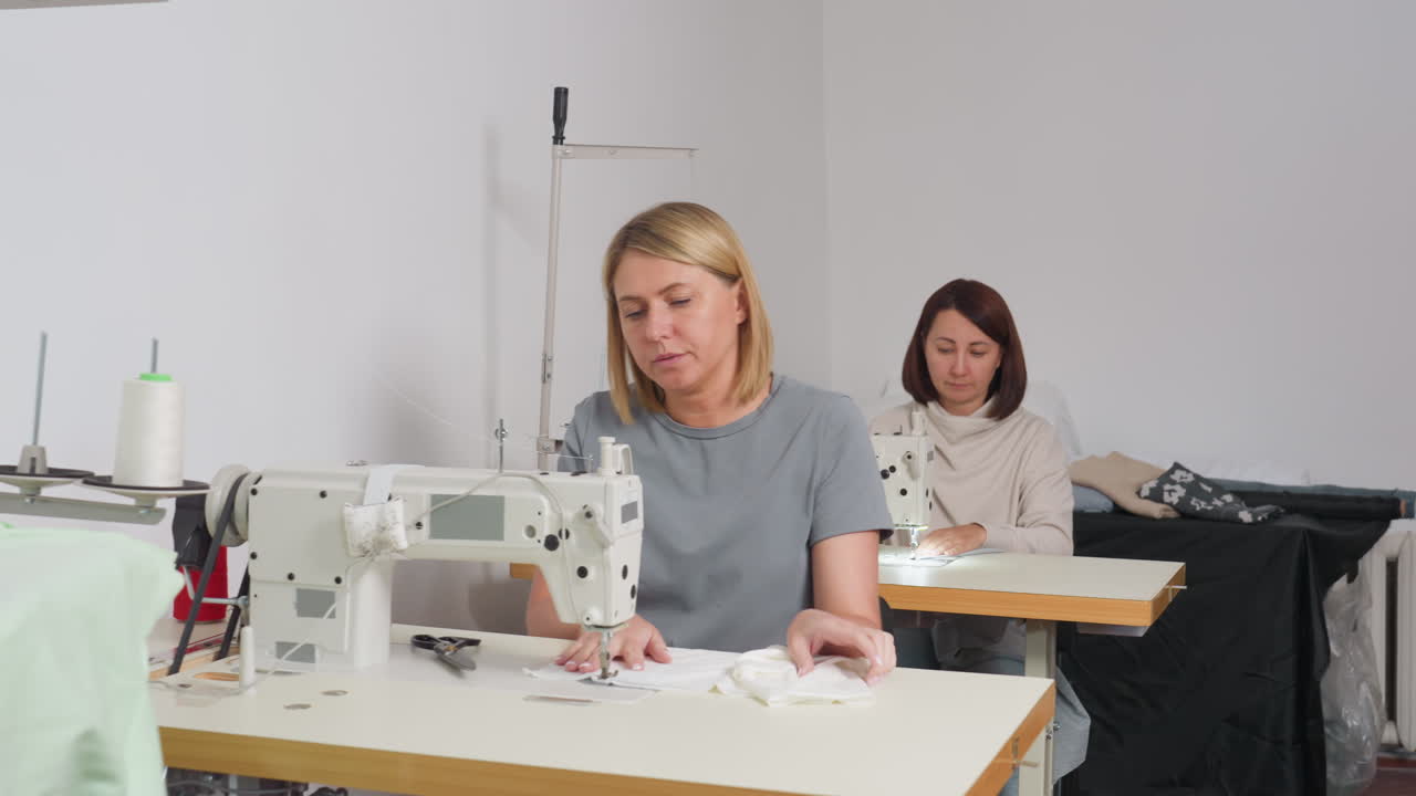 Fashion designers meticulously arranging bright white fabrics on sewing machine in minimal workshop setting, showcasing professional skill, collaboration, concentration, and garment creation process