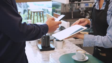 hands of customer using smart phone scanning qr code for paying to cashier at cafe, staff using tablet while client payment with internet banking, business and technology about transaction concept.