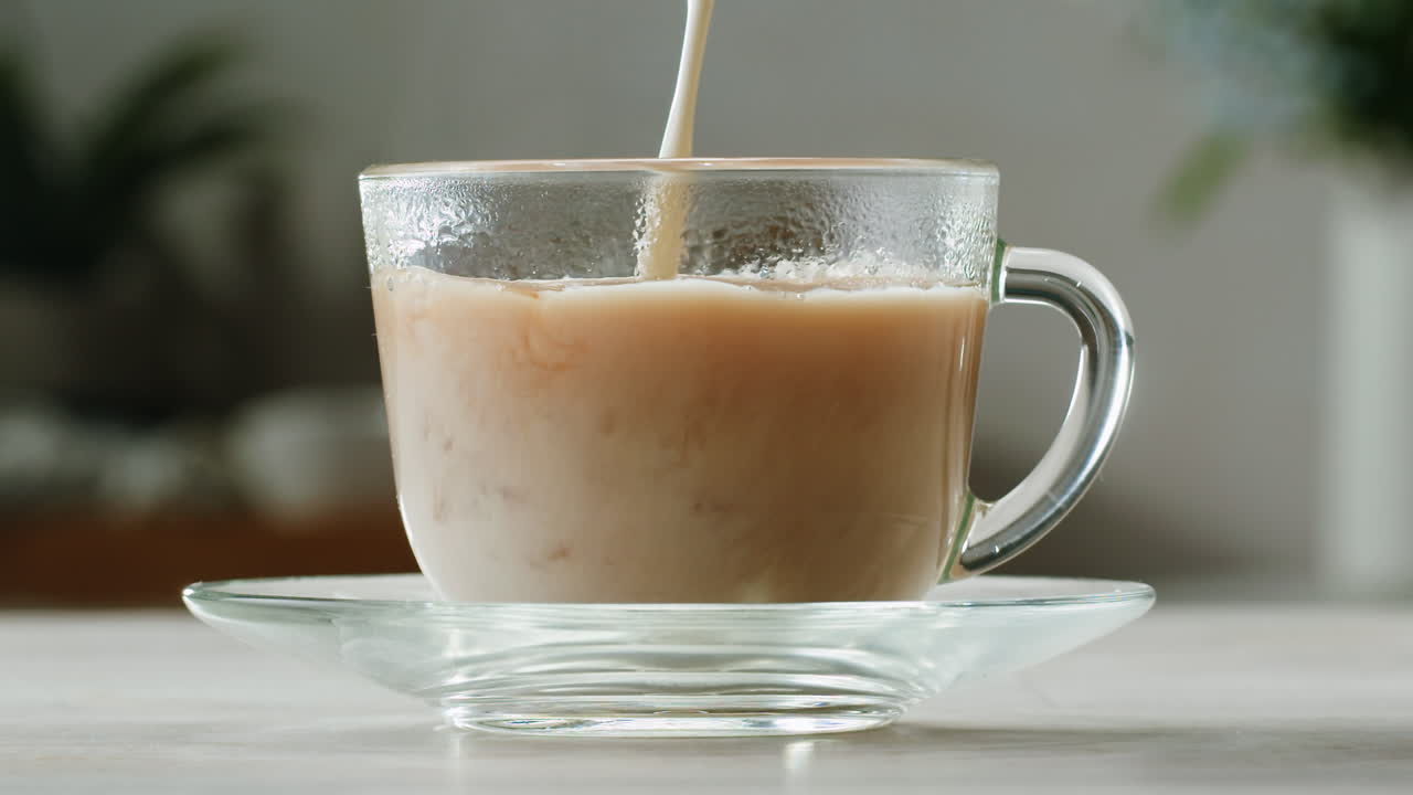 Pouring milk into black tea in glass cup. Drinking hot tea with milk, healthy morning, freshly brewed detox drink. High quality 4k footage
