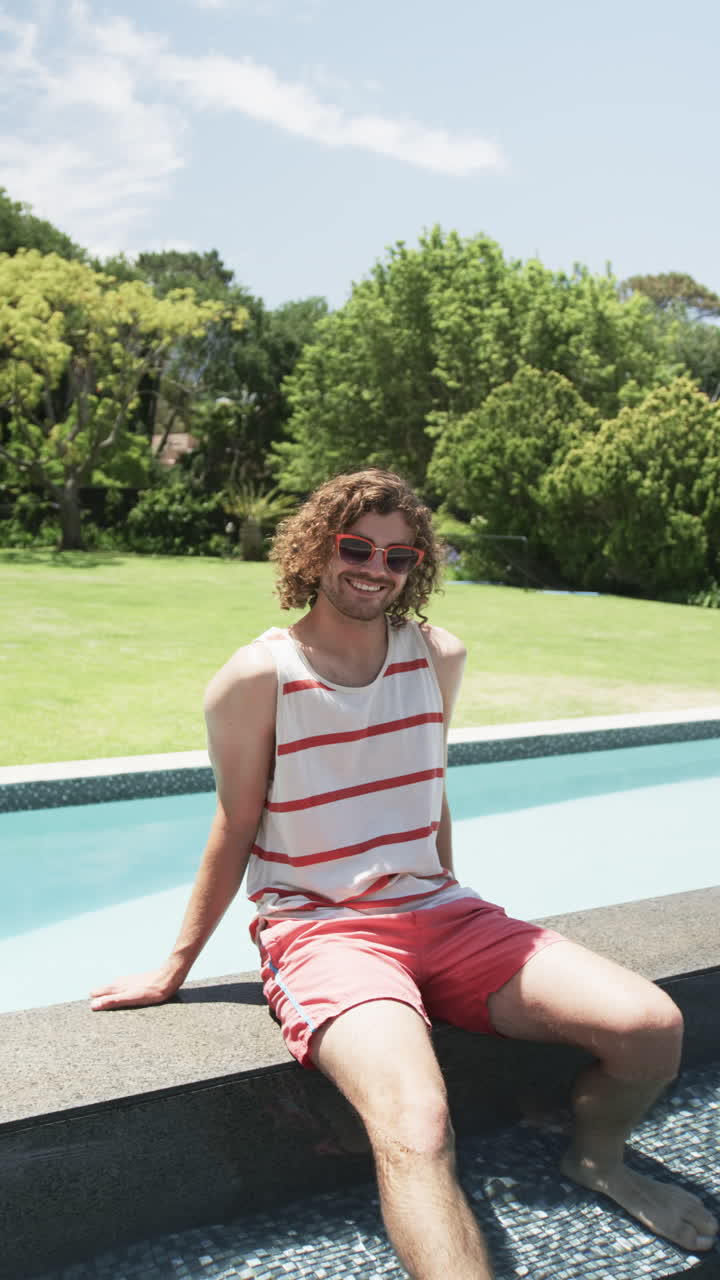 Vertical video: Caucasian young man sitting by pool, smiling, at home