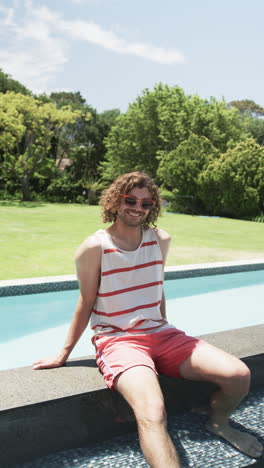 vertical video: caucasian young man sitting by pool, smiling, at home