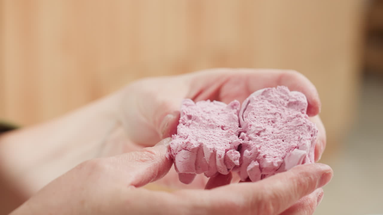 Close up of chef holding soft pink cupcake gently pressed and split in half to reveal fluffy texture with playful hand gesture and blurred kitchen background