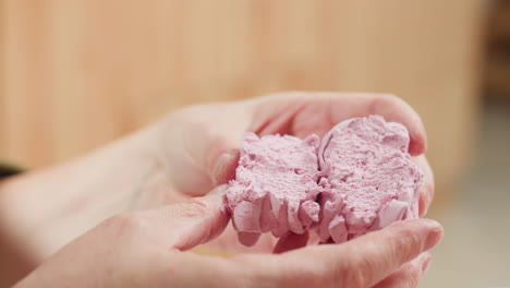 close up of chef holding soft pink cupcake gently pressed and split in half to reveal fluffy texture with playful hand gesture and blurred kitchen background