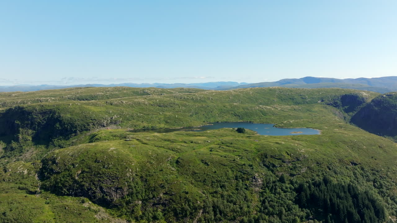 Aerial footage approaching a serene lake on Vidden above Bergen, with distant mountains and plateau in view