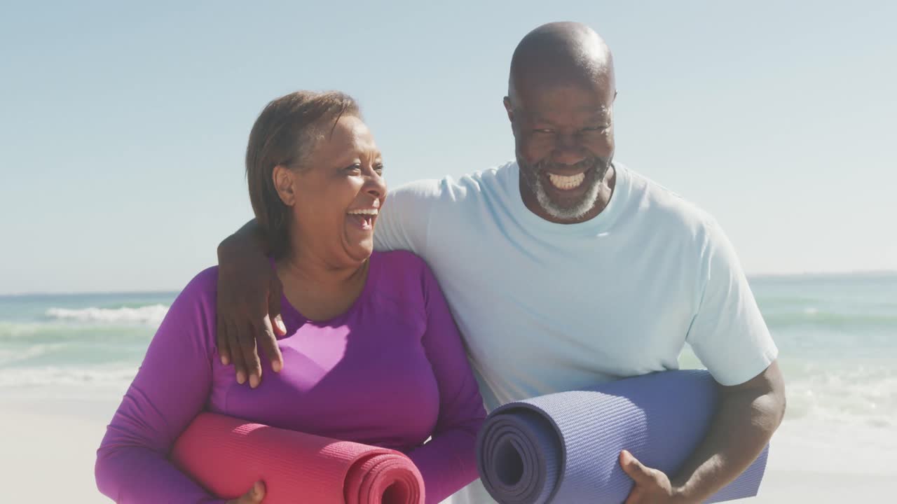 retrato de una feliz pareja afroamericana de alto nivel con esteras de yoga en una playa soleada