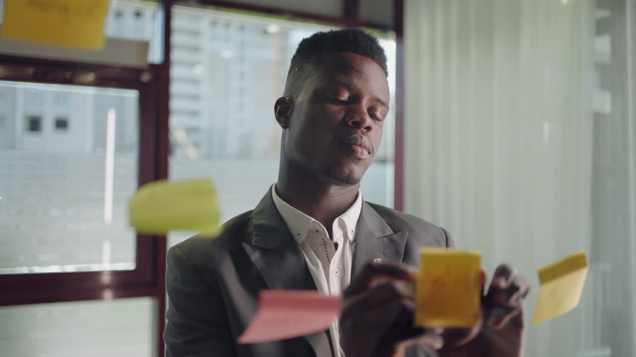 African american business man using sticky notes brainstorming problem solving strategy on glass whiteboard leader man Planning Project On Post It Sticky Notes in office.