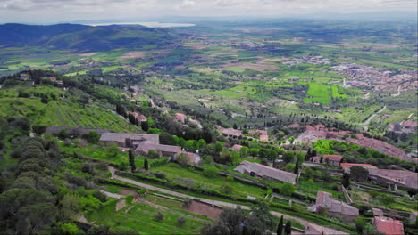 Hilly-farmland-and-small-old-town-of-Cortona-in-Italy,-forward-aerial