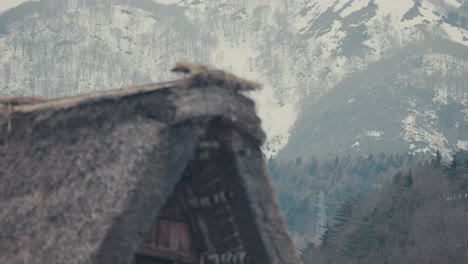 traditional gassho-zukuri style house and snowy mountains in shirakawa-go village in shirakawa, japan