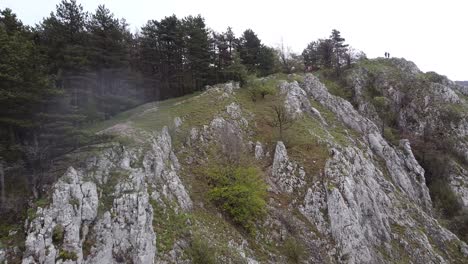 Finden-Sie,-Wonach-Sie-Suchen---Ein-Reisender-Mit-Rucksack,-Der-Die-Spitze-Einer-Steilen-Bergklippe-Mit-Flachen,-Farbigen-Waldhügeln-Erreicht