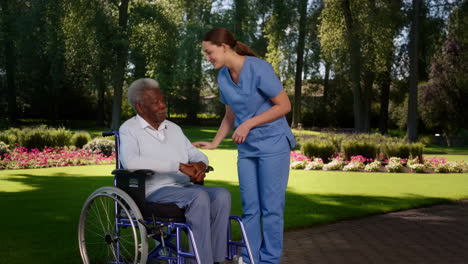 a caregiver assisting an elderly man in a wheelchair in a park
