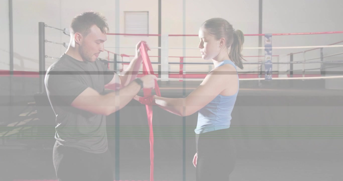 Trainer feeding red hand wrap and winding around trainee hand in boxing ring, securing for sparring