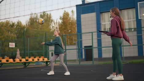 newbie practicing volleyball serve, being observed by coach with performance book in hand and whistle in mouth, monitoring technique on outdoor court