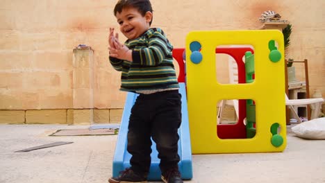 Cute-two-years-old-boy-dirty-from-the-cookies-around-the-mouth-sliding-down-the-plastic-slide-play-house-in-backyard