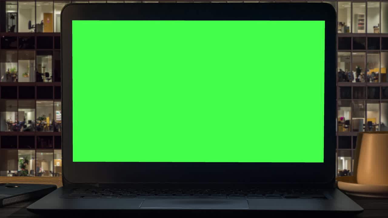 A black laptop with a green screen against the background of office windows.