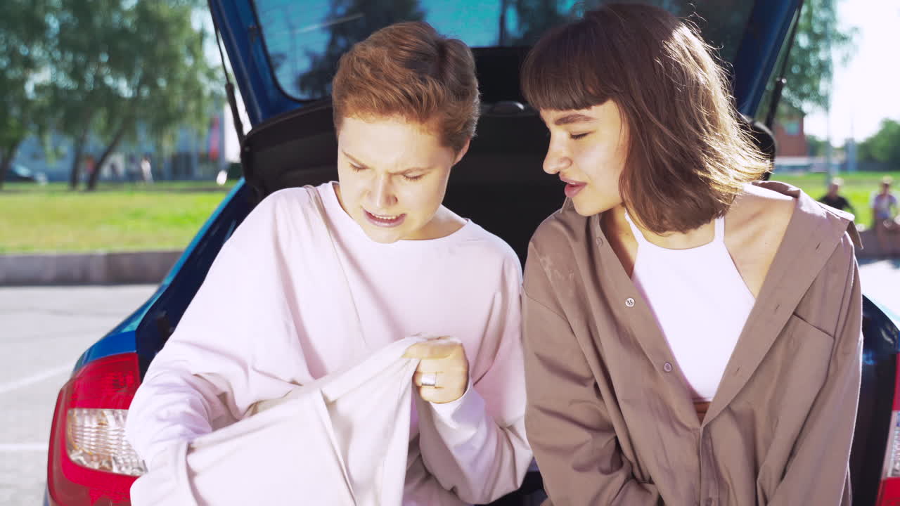 두 명의 여성이 자동차 트크에 있는 가방을 보고 있습니다.