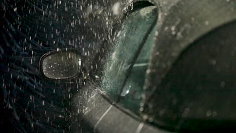 from the interior perspective, a handheld camera focuses on a car's rectangular side mirror, in a bustling car wash framed by blue bristles and dancing water droplets