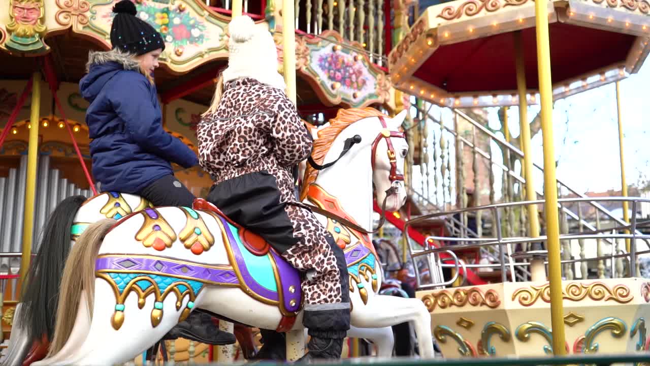 Young children ride colorful old-fashion carousel horses side by side, Tivoli Gardens, Copenhagen, Denmark, close up slow motion pan