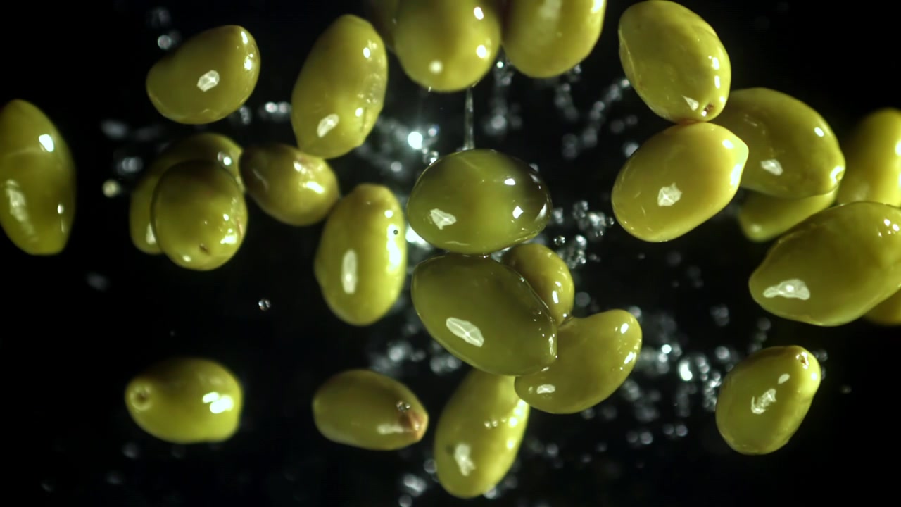 Movimento rallentato di olive verdi che schizzano acqua su sfondo nero