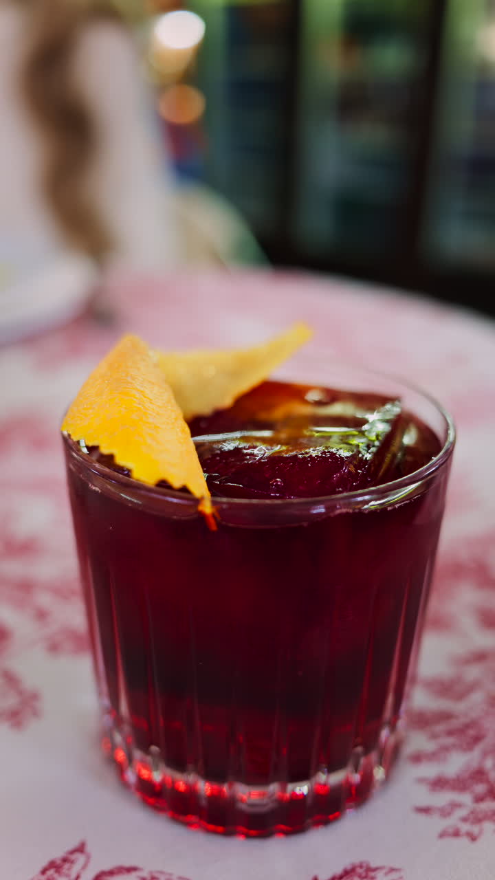 Close up of a negroni cocktail on a red and white tablecloth at a restaurant. Vertical