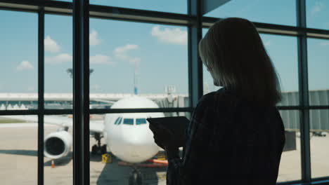 silueta de una mujer de negocios junto a la ventana de una terminal de aeropuerto usa una tableta digital