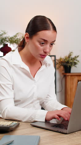 young businesswoman manages budget in laptop spreadsheet clicks physical calculator and checks sums
