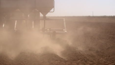 close up of a plow tilling the field while its dry and kicking up a cloud of dust