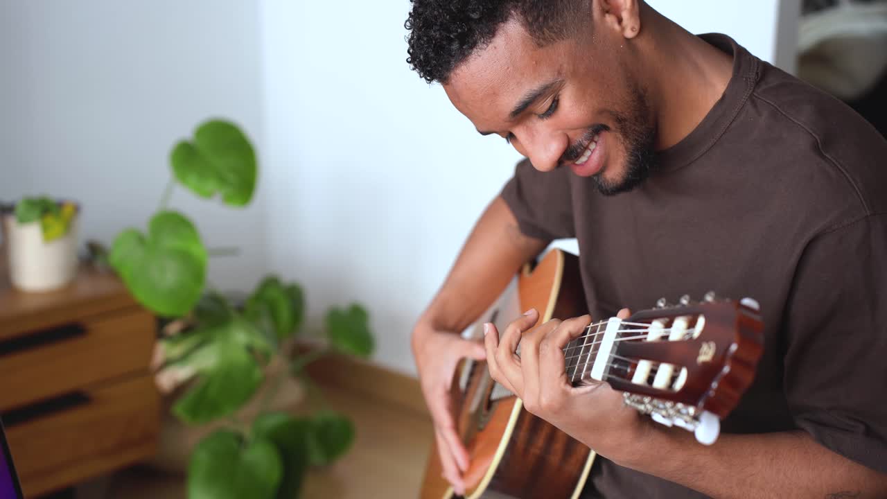 hombre étnico sonriente tocando la guitarra acústica en casa