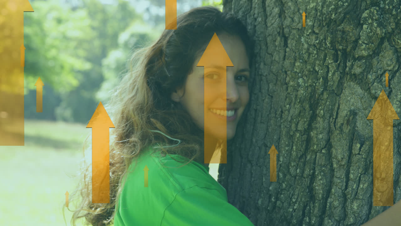 animación de flechas amarillas sobre una feliz mujer caucásica abrazando un árbol