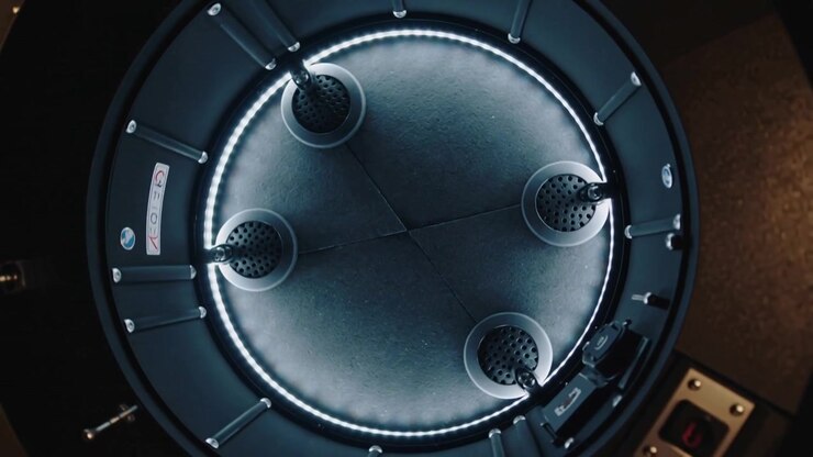 Rotating circular metal chamber revealing moving nozzles, glare on bench with power switch flipping