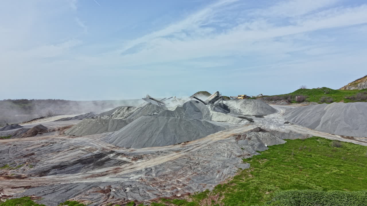 Sito di cava di granito con grandi cumuli di pietra e attrezzature sullo sfondo durante le ore diurne.