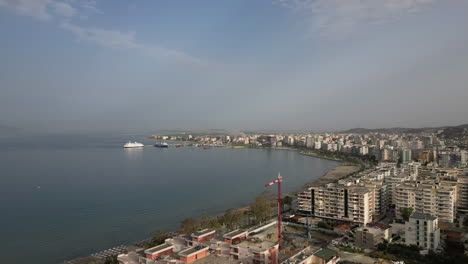 drone disparó hyperlapse por encima de la ciudad vlore albania mirando sobre los edificios y el puerto con el ferry con el mar y la playa por debajo en un día soleado con un poco de neblina registro