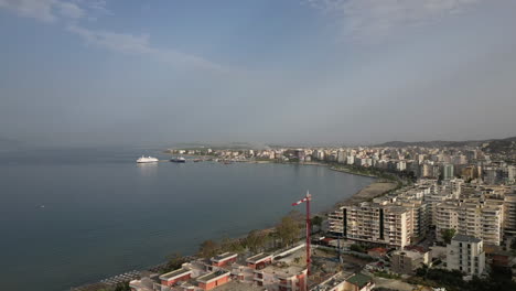 drone shot hyperlapse above the city vlore albania looking over the buildings and harbour with ferry with the sea and beach underneath on a sunny day with a little bit of haze log