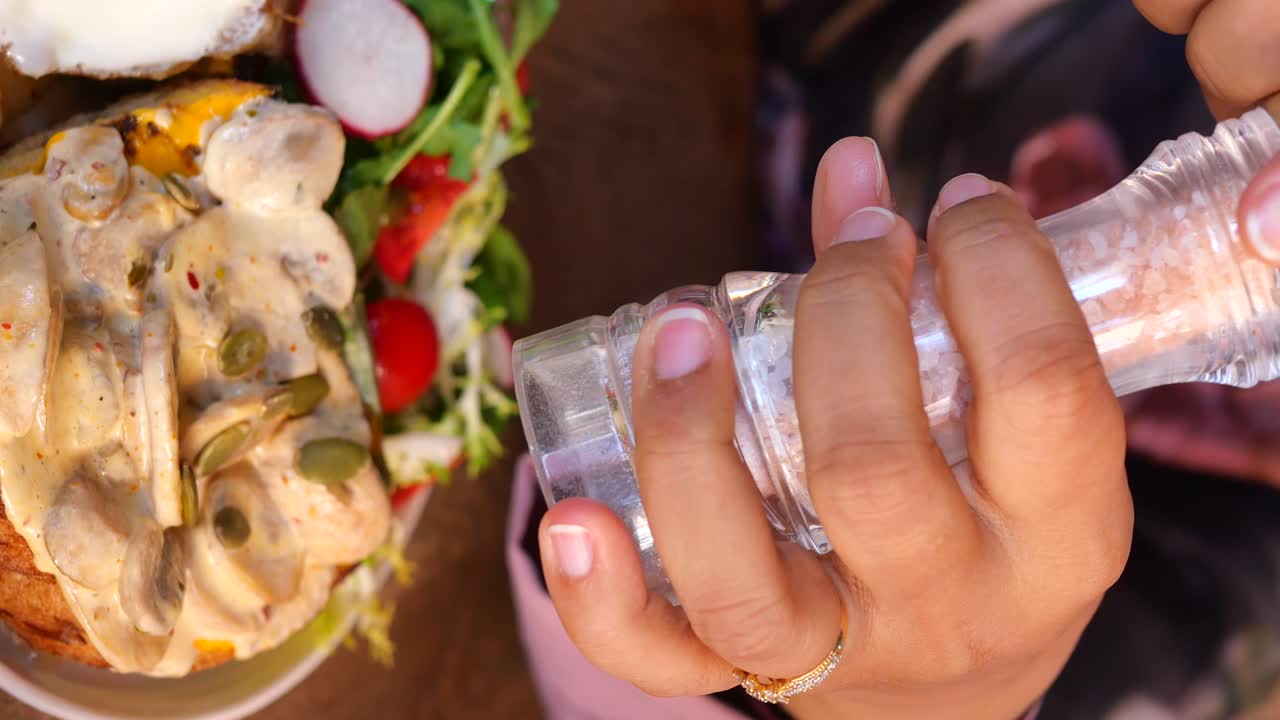 mujer sazonando su comida con sal y pimienta