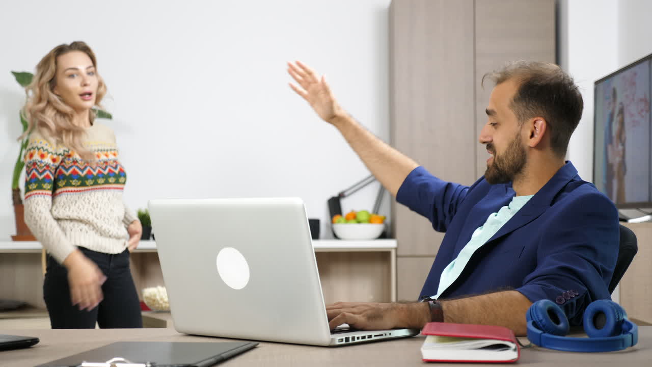 Man working on laptop in office with woman nearby