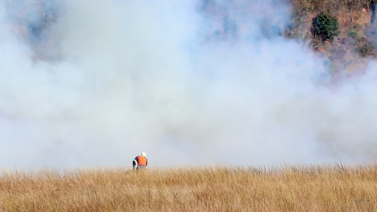 Native fire fighter working on fire break as smoke flies over field on farm