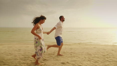 Joven-Pareja-De-Enamorados-En-Ropa-Ligera-Sin-Preocupaciones-Corriendo-En-Una-Playa-Tropical-Limpia