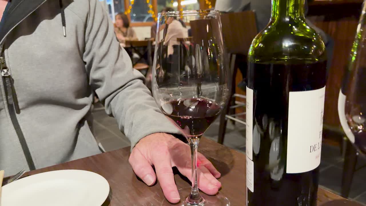 Primer plano de un hombre apoyando su mano cerca de vino tinto en un restaurante japonés