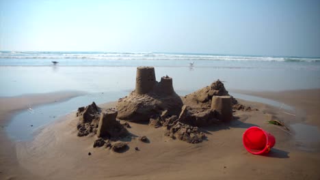 Completed-sandcastle-on-the-beach-with-waves-crashing-behind