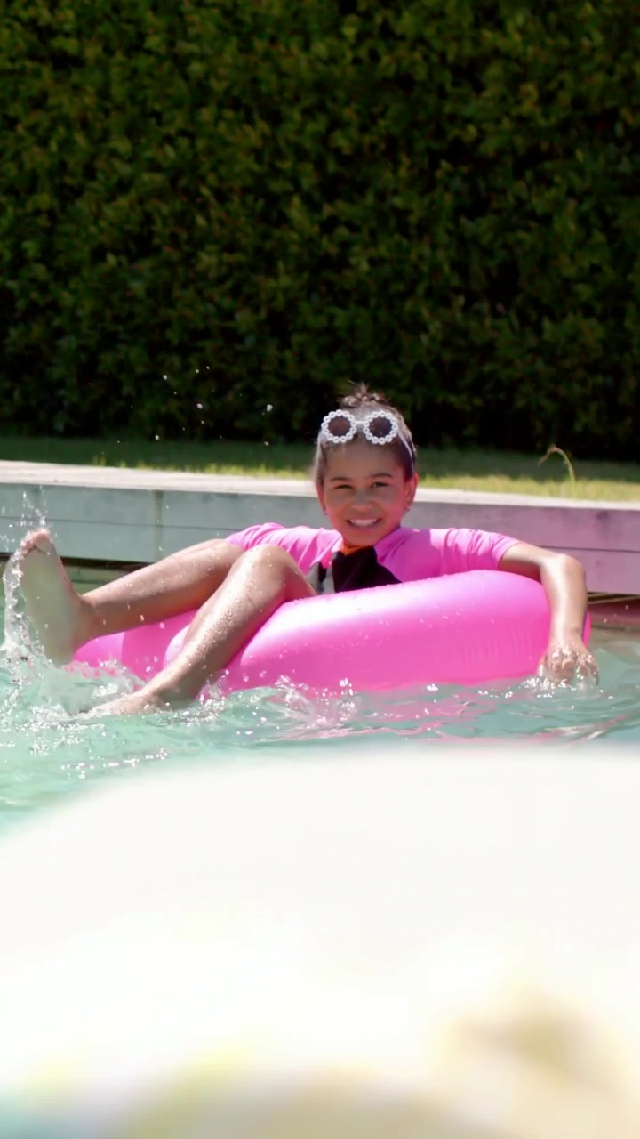 Vertical video: Shifting sending girl in pink top kicking, steering ring at pool, pushing up shades