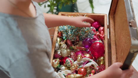 partial view of boy in casual wear opening old box filled with colorful shiny ornaments near christmas tree, carefully preparing decorations in cozy indoor setting with soft holiday atmosphere