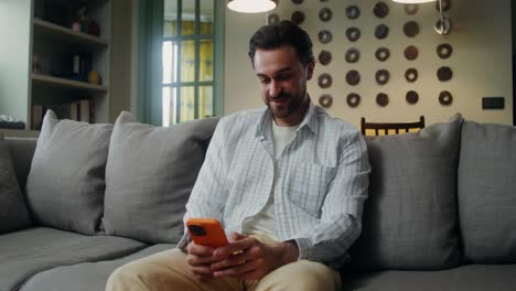 hombre usando un teléfono inteligente en un sofá en una sala de estar