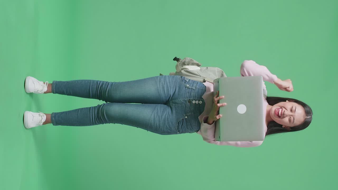 cuerpo lleno de estudiante mujer asiática usando computadora portátil y celebrando en el estudio de pantalla verde