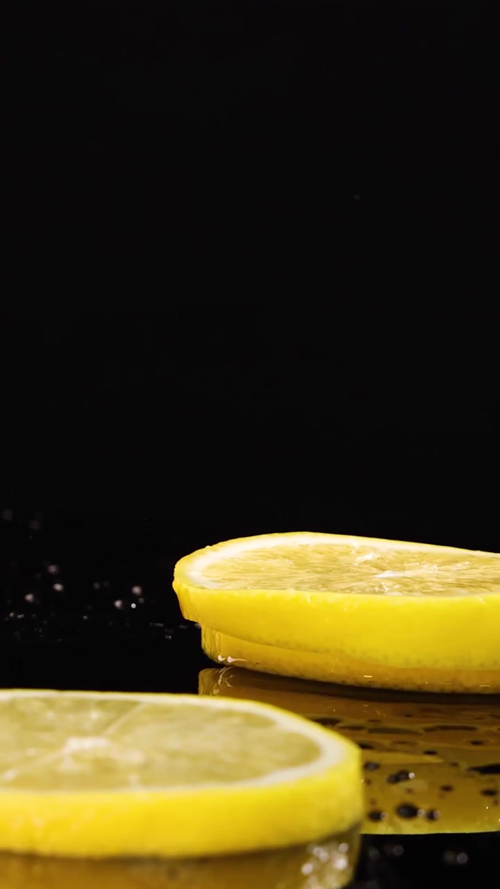 Sottili fette di limone cadono e rimbalzano su una superficie bagnata riflettente su uno sfondo nero, catturate ad alta velocità con illuminazione drammatica e dettagli nitidi