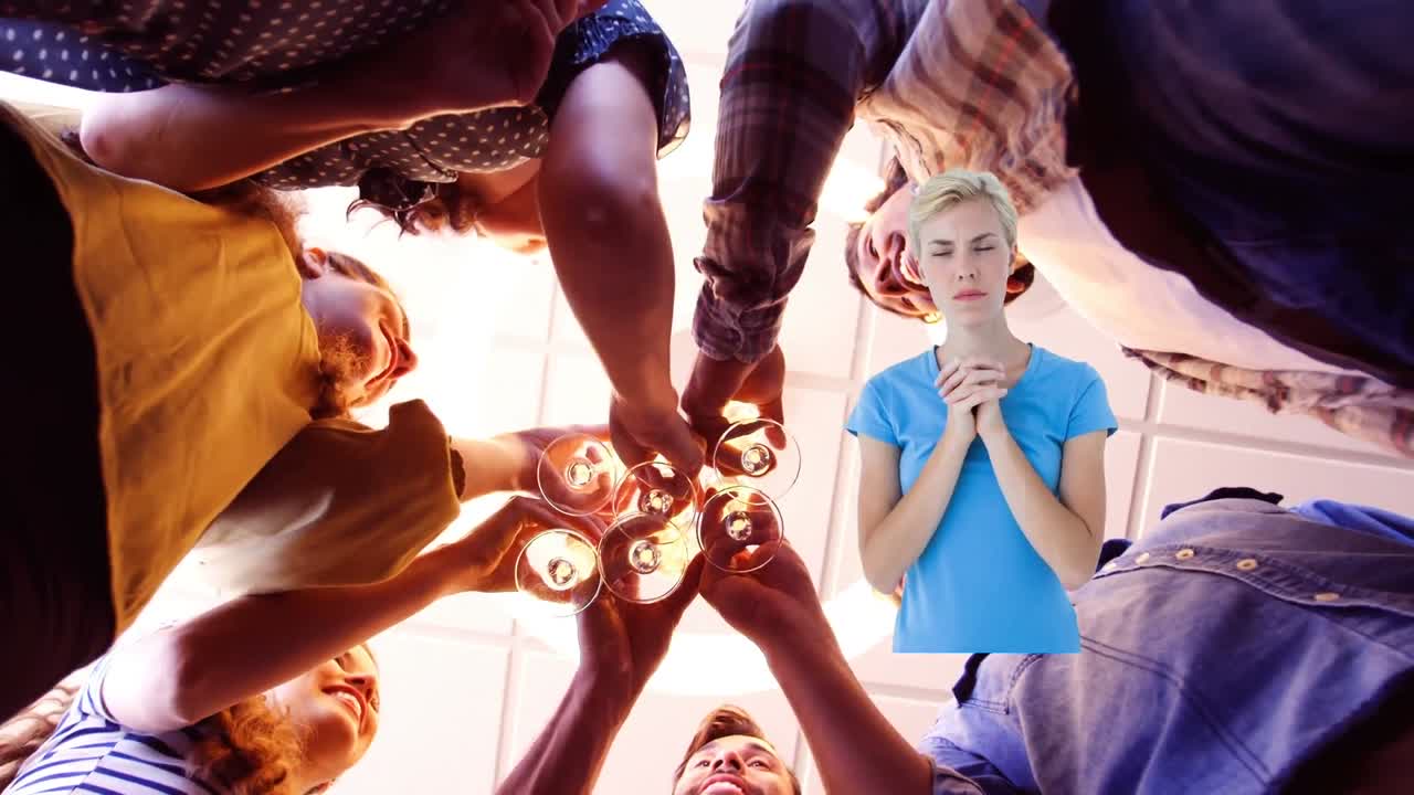 mujer caucásica orando sobre vista de ángulo bajo de diversos colegas de oficina brindando sus bebidas