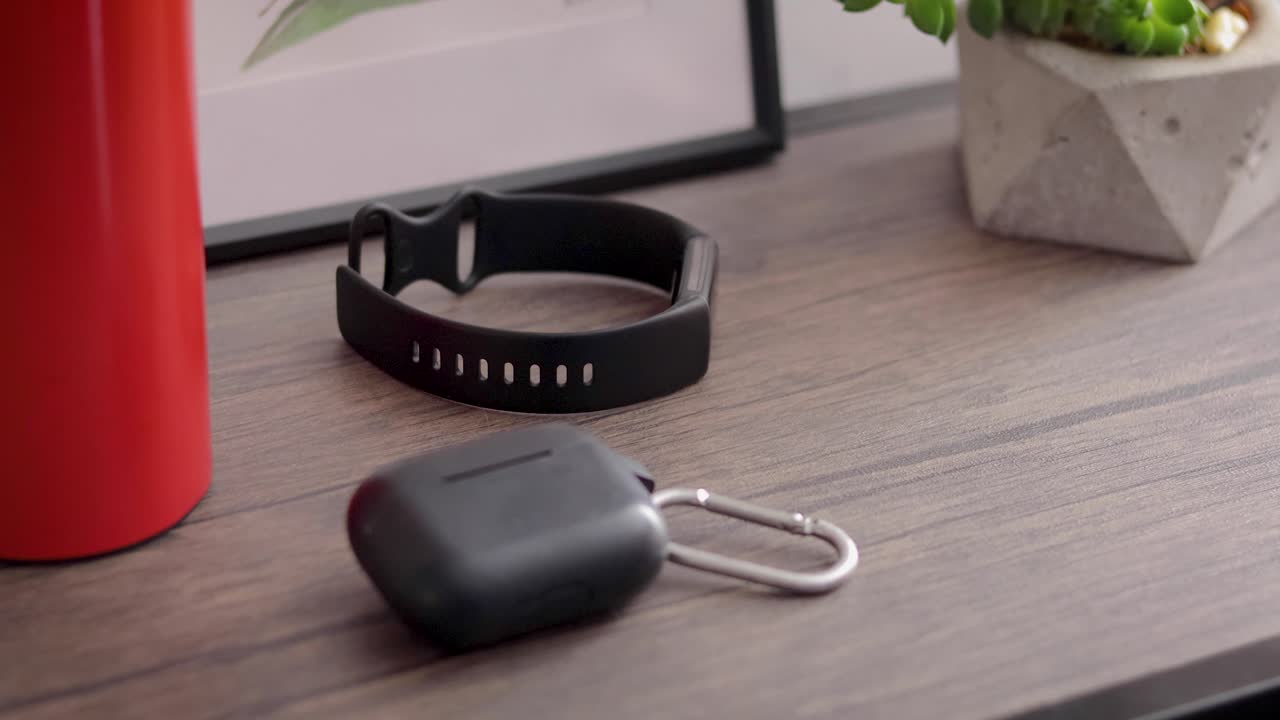 un hombre tomando su teléfono celular, auriculares, reloj inteligente y botella de agua de una mesa decorada con acuarela y planta
