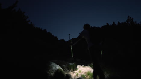 camera shot from behind of a hiker climbing up a mountain with his headtorch to illuminate his path towards the top