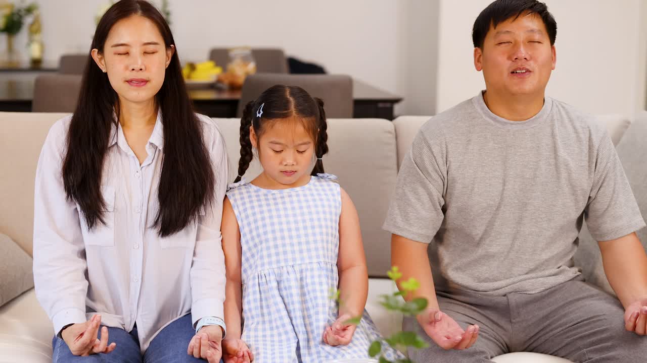 Three family members practice mindfulness meditation, seated on sofa, natural daylight, calm atmosphere