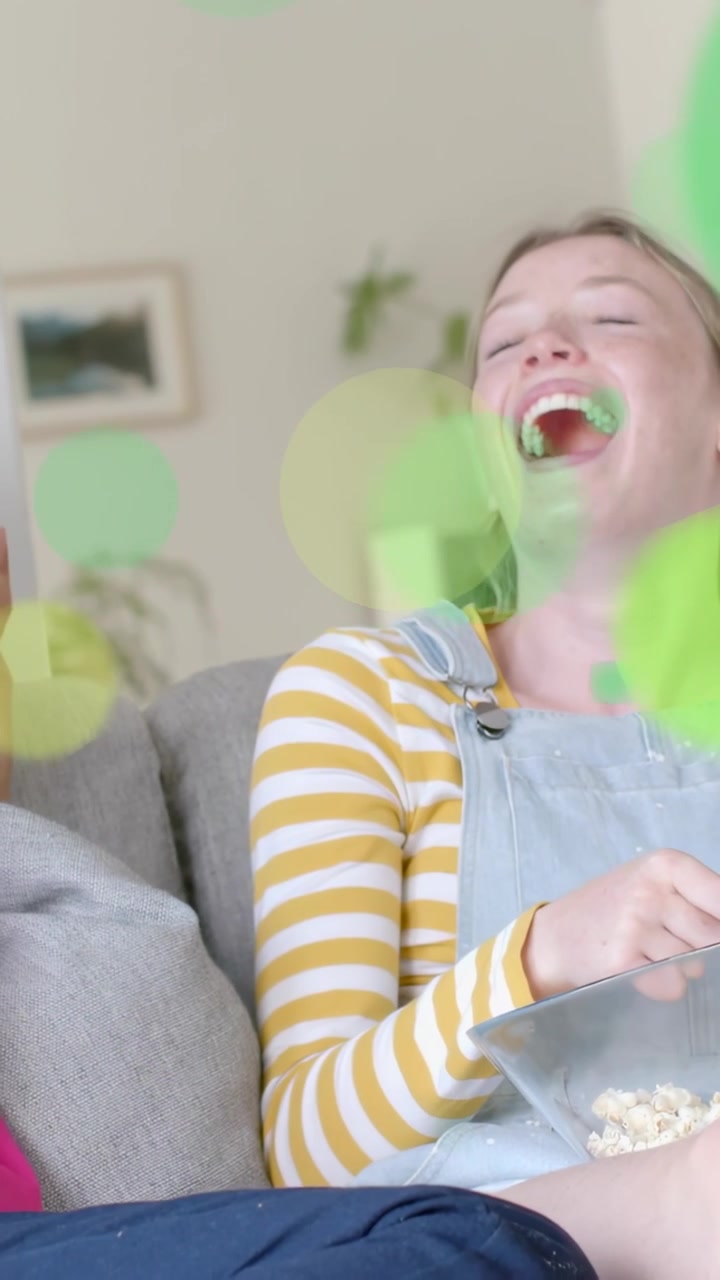 Vertical video: Social left hand sharing popcorn they laughing green circles drifting over them